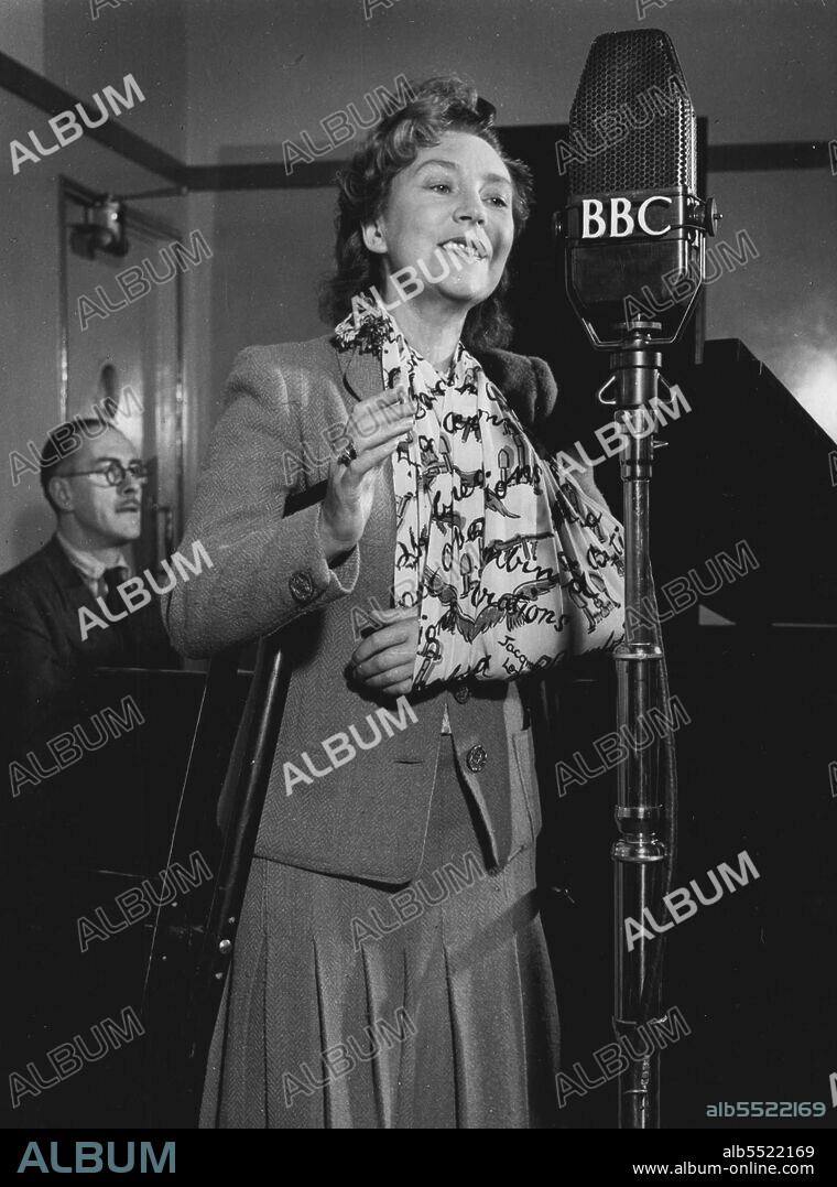 Annette Mills returns to broadcast a programme of her own songs in the BBC Forces Programme, on November 3rd, 1943. She is accompanied at the piano by Rex Burrows (in the background).Annette Mills, the dancer who introduced the Charleston to Great Britain, and the composer of 'Boomps-a-daisy', has been in hospital for a year following a serious motor accident which occurred while she was driving between two R.A.F. stations to entertain the airmen. She suffered eight fractures, and is still dependent upon crutches and a sling. On November 4th, the day after this broadcast, she returns to hospital for what she hopes will be her final operation. November 03, 1943. (Photo by BBC).