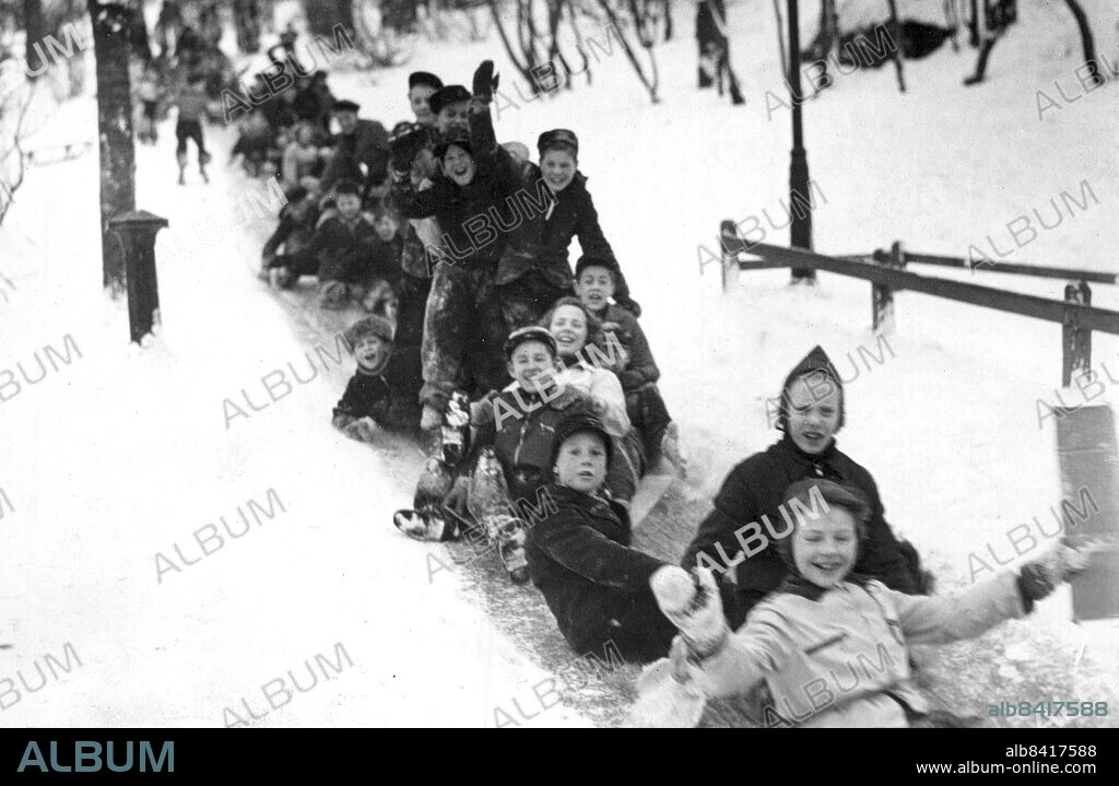 Stockholm 1940-02-07. Vinter i Stockholm. Tövädret och den påföljandekylan har skapat ett extra tivoli och barnens paradis på söder. Backen vid Högalidskyrkan förvandlades i ett slag till en 100 meter lång härlig kana. Man sätter sig helt enkelt på baken och så rutschar man i väg allt vad tyget håller. Glidet är glänsandeoch skolan stängd på grund av koksbristen. Härliga tider, strålande tider. Mammorna på Söder som fått extra bekymmer med stoppning av byxbakar och pressning av kappor fundera emellertid efter onsdagens stora sportevenamang, Södermästerskapet i skinnkälke, allvarligt på att ringa renhållningsverket och rekvirera ett lass sand.. Foto: DN / TT / Kod: 192. ** SvD OUT **.