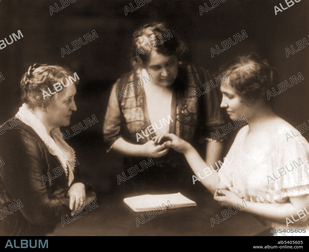 Helen Keller reading a woman's fingers as another woman watches. The image shows communication using the manual alphabet for finger spelling. Photographed by Gerhard Sisters, 1914. Helen Keller (1880-1968) was an American author, political activist, and lecturer. She was the first deaf-blind person to earn a Bachelor of Arts degree. The story of Keller and her teacher, Anne Sullivan, was made famous by Keller's autobiography, The Story of My Life, and its adaptations for film and stage, The Miracle Worker. A prolific author, Keller was well-traveled and outspoken in her convictions. A member of the Socialist Party of America and the Industrial Workers of the World, she campaigned for women's suffrage, labor rights, socialism, antimilitarism, and other similar causes.