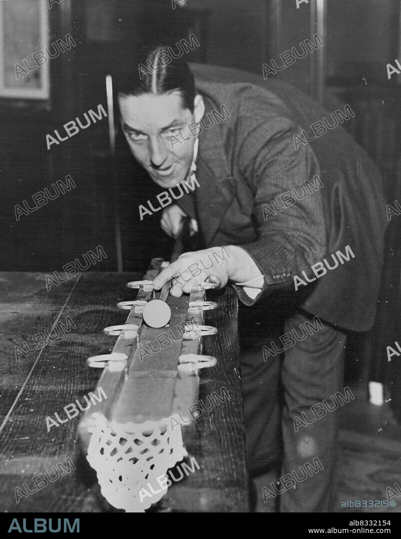 Tom Newman Plays New Billiards Game - Tom Newman the famous billiards player, tries his hand at the new game "Snukapool" at Thurston's. The game may be played by any number of persons, and consists of a strip of billiards table with nine pockets. Each pocket has a hazard in front of it and is numbered from naught upwards with a groove near the top of the table which scores fifty if the player cues the ball into it. The player continues to make his break untill he fails to score, either by  "'potting" a naught of failing to put the ball down. The top pocket is naught. January 12, 1937. (Photo by London News Agency Photos Ltd.).