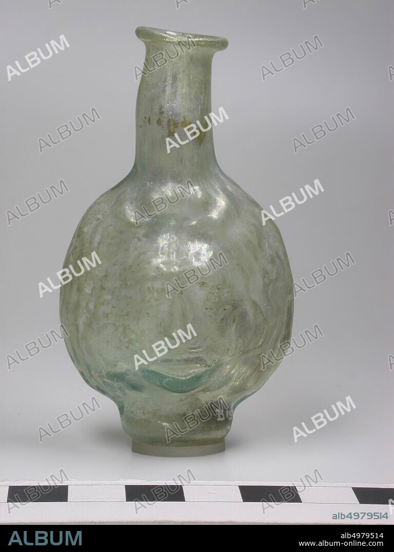 Thin-walled Janus cup bottle for perfume. From two halves of colorless to green glass blown, add visible. Flat mouth rim and a free blown neck that is slightly crooked. Torus socket, flat at the bottom, bottles in the form of a human face appear for the first time in the 2nd century AD. They are blown into a shape and usually have the characteristic of a 'janus head', a face on the front and back. Rarely are the vases that have been worked out like a head around., Crockery, glass, H 8 cm, Russia.