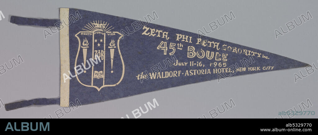 The Zeta Phi Beta Sorority was founded in January 1920 at Howard University,  historically black research university, in Washington, D.C. This triangular shaped felt pennant is a faded royal blue on the front. It has a white stripe along the one short straight edge, and white lettering that reads "ZETA PHI BETA SORORITY Inc. / 45th Boule/ July 11-16, 1965/ the Waldorf-Astoria Hotel, New York City." To the left of the letters is the sorority crest. This depicts a shield shape with fourteen rays emanating from the top. The shield itself is divided into three fields. The two outermost fields show lit torches, while the middle field shows the three Greek letters of the sorority, under three stars, and over an open book with the date 1920. There are two blue felt strings attached to the white strip along the short side of the pennant.