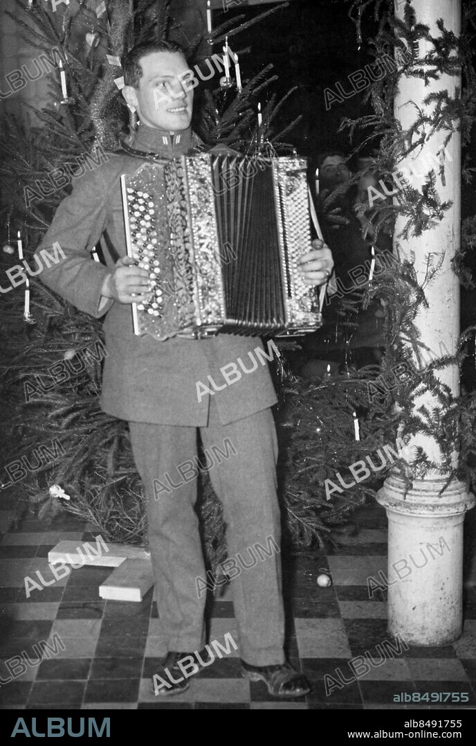 TYSKLAND BECKINGEN 1934-12.. Orig. bildtext... SVENSK JUL I SAAR. Sala-bon Södergren klämmer i med Dubbelörnen vid julgranen i Beckingen. Not. Dragspelare Södergren vid julgranen i Beckingen. Anm. Från 1919 förvaltades Saarområdet av Nationernas Förbund. 1935 hölls en folkomröstning om området skulle tillhöra Tyskland. Folkomröstningen leddes av en neutral kommission under svenskt presidium; ett svenskt kompani ingick också i den internationella styrka som övervakade valet. Efter folkomröstningen återförenades området med Tyskland. Se även BBQ363-BBQ365, BBV487-BBV490 och BBV492 Bildserier Fotoreportage Dragspel Julfirande Julgransljus CD573 sites: BECKINGEN;SVERIGE*;SAAROMRÅDET;TYSKLAND.