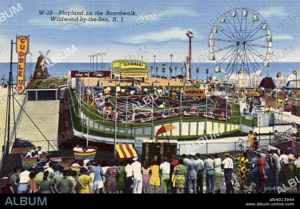 Playland amusement park on the Boardwalk, Wildwood-By-The-Sea, New Jersey, USA, 1940. Postcard. View of Playland showing the Cuddle Up, Skooter, and Caterpillar rides. A Ferris Wheel and the ocean are visible in the background. Many people watch and ride the attractions.