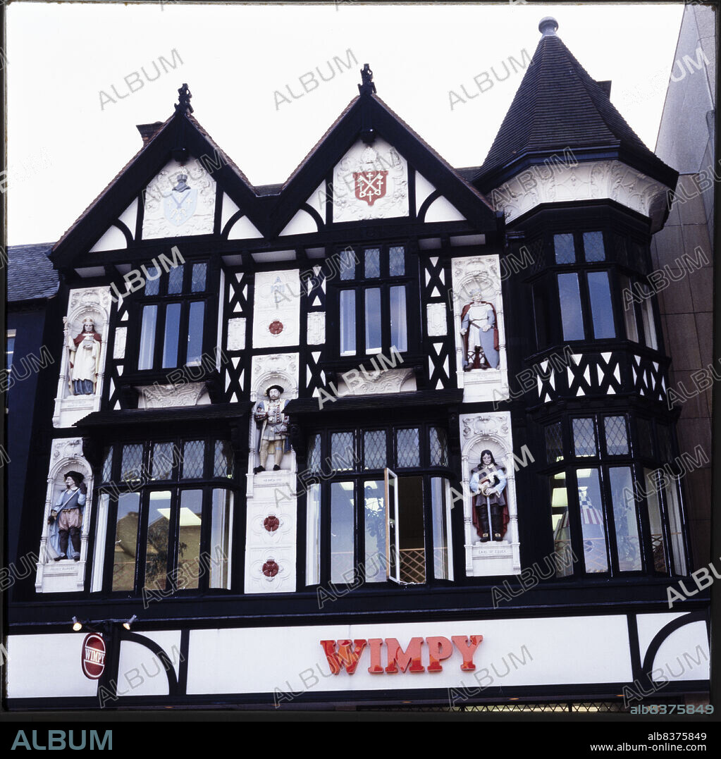 NICHOLAS ANTHONY JOHN PHILPOT. Cathedral Square, Peterborough, City of Peterborough, 1970s-1990s. The half-timbered upper elevation of 8 Cathedral Square, built as a Boots store, with painted statues in niches flanking the upper floor windows. The Boots store in Cathedral Square was is dated 1911, and was designed by Boots' in-house architect Michael Vyne Treleaven. The statues on the facade were sculpted by Gilbert Seale & Son of Camberwell, London, and depict Athelwold, King Peada of Mercia, Henry VIII, Prince Rupert and the Earl of Essex. The premises were later occupied by Wimpy and Burger King restaurants.