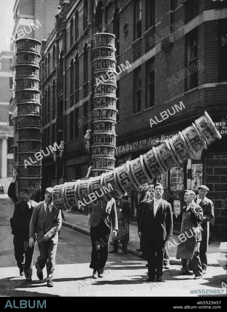 Leaving Tower Of Baskets Comes Tumbling Down -- A Covent Garden Market (London) porter can carry twelve baskets tower-style on his head indefinitely: it's the porters tradition. But in a race, it's a different matter, and even Albert Bailey of Highbury, London, basket race winner in the last event held in 1939, comes to a mishap. Occasion is rehearsal in Covent Garden today (Saturday) for the event to be held during the Covent Garden Market Show later this month. Between 20 and 30 contestants are entered from London's mix who lesale markets. With Bailey in photo are Edward White of Blackheath (left) and Johnny Hopkins of Finsbury Park. June 02, 1951. (Photo by Reuterphoto).