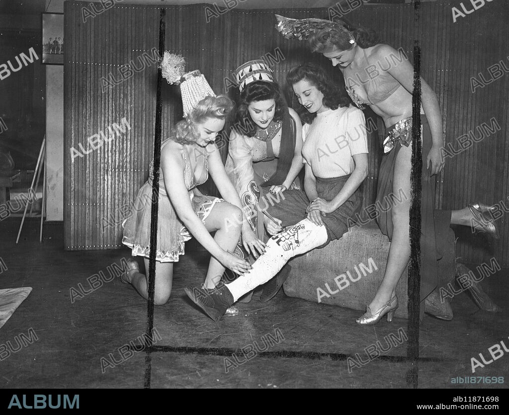 Jennifer Clarkson a young showgirl at London's Windmill Theatre, slipped and fell downstairs as she came off stage, breaking her leg. Now her colleagues insist on using the plaster encasing the injury as a useful surface for the inscription of Christmas greetings. Picture shows: left to right Elizabeth Kearns, Jill Austey, Jennifer Clarkson and Lesley Lorne at the Windmill Theatre. 22 December 1946.
