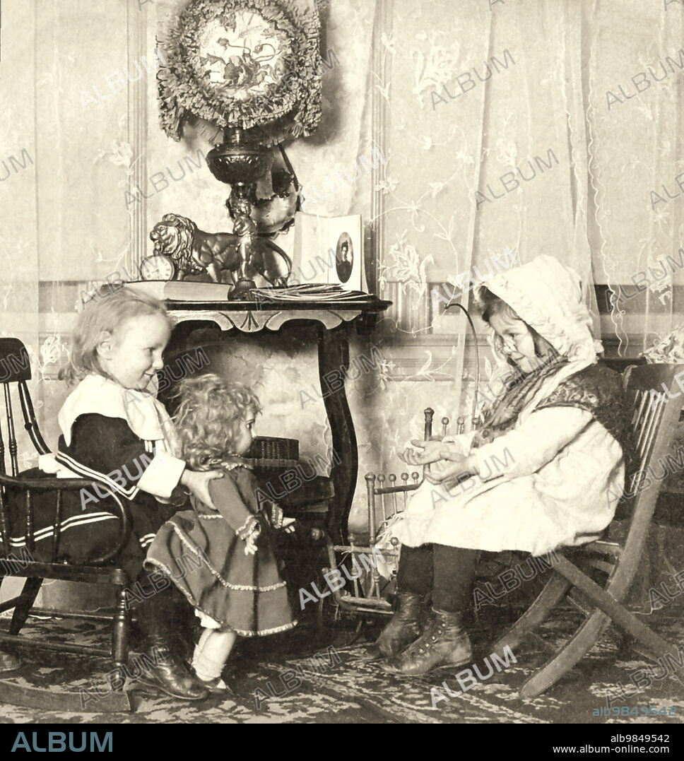Victorian Stereoview card from circa 1900 for viewing thought a stereoscope. Two little girls playing with a doll, one dressed as a mummy and the oither as grandma beconing the doll to come to her. The slide title is Ã¢â‚¬Å“Bless her little heart,come to Grandma Ã¢â‚¬Å“.