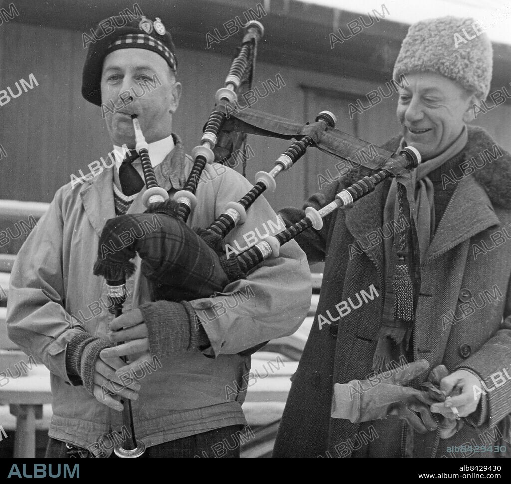 STOCKHOLM 1960-11-13.. En svensk-skotsk curlingtävling går av stapeln på Tennisstadion. Mr. George Reid har tagit med sig sin säckpipa och här lyssnar f.d. svenske mästaren Hubertus Ubbens med nöje till välljudet.. Foto: AB Text & Bilder / SVT / Kod: 5600. Mapp: Svensk curling I:34 1/2A. Säckpipor Kepsar Mössor.