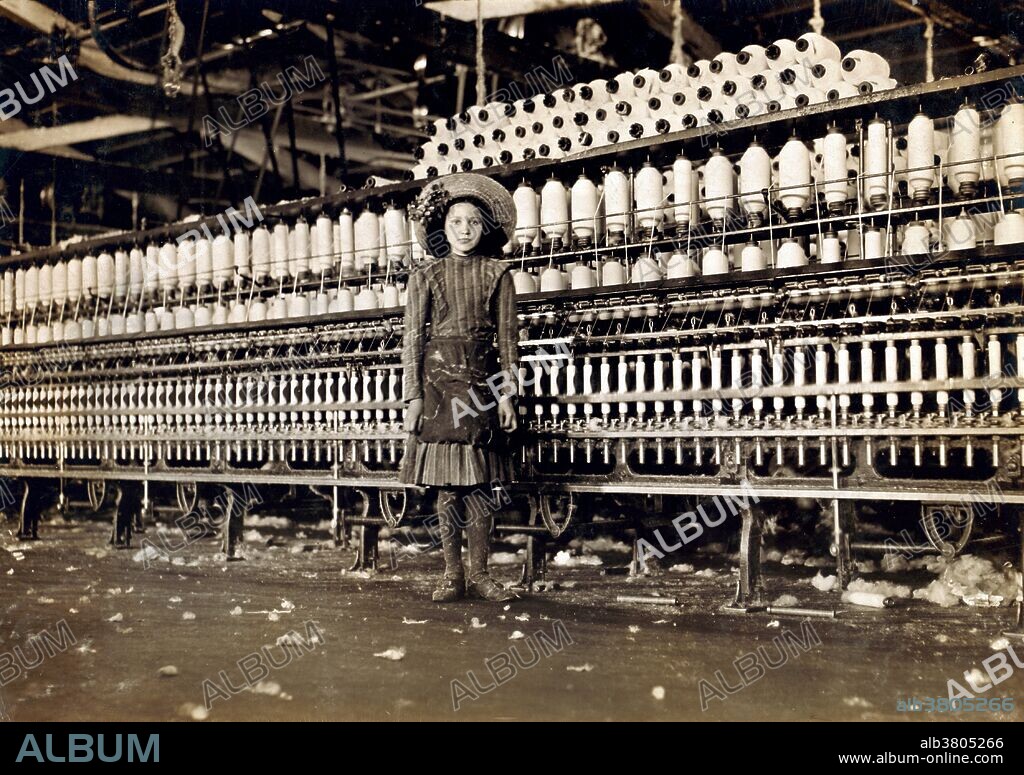 Entitled: "Young spinner in Roanoke Cotton Mills. Said fourteen years old, but it is doubtful. Location: Roanoke, Virginia." Cotton mills were designed to move cotton through a precise series of production processes that separated, straightened, and twisted cotton fibers, combined them into yarn, then wove the yarn into cloth. Workers directed four or more slivers through a series of rollers in the head of a drawing frame, where they were combined in a single strand. As bobbins on the spinning frames filled with thread, doffers replaced them with empty ones. The spinner's job was to move quickly up and down a row of machines, repairing breaks and snags. Child labor refers to the employment of children in any work that deprives children of their childhood, interferes with their ability to attend regular school, and that is mentally, physically, socially or morally dangerous and harmful. Photographed by Lewis Hine, May 1911.