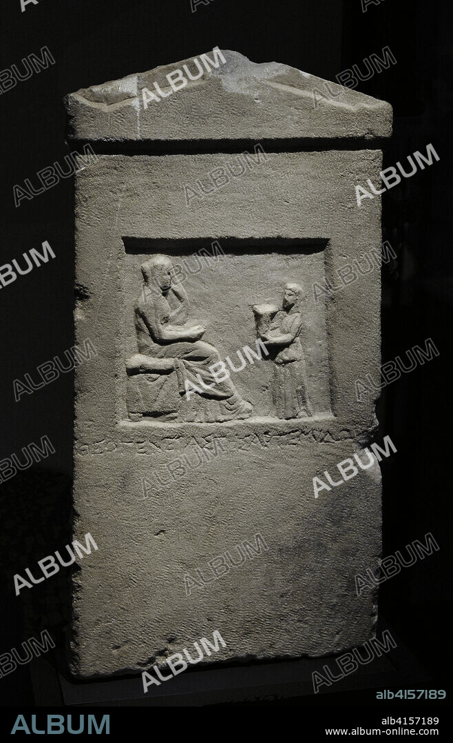 Estela de Teogeneta. Estela funeraria de época helenística. Procedente de alguna ciudad griega de Asia Menor, muestra en bajo relieve la escena funeraria. Debajo de ella, la inscripción dedicatoria: "Theogenetas tis Artemidorou" ("Teogeneta, hija de Artemidoro"). La difunta aparece sentada sobre un asiento con almohadón, dirigiendo su atención hacia una figura femenina de menor tamaño, posiblemente una sirvienta, que le ofrece un kálathos (cesta en la que las mujeres guardaban los copos de lana para hilar). Siglo III a.C. Mármol. Altura: 57,5 cm; anchura: 30 cm. Museo Arqueológico Nacional. Madrid. España.
