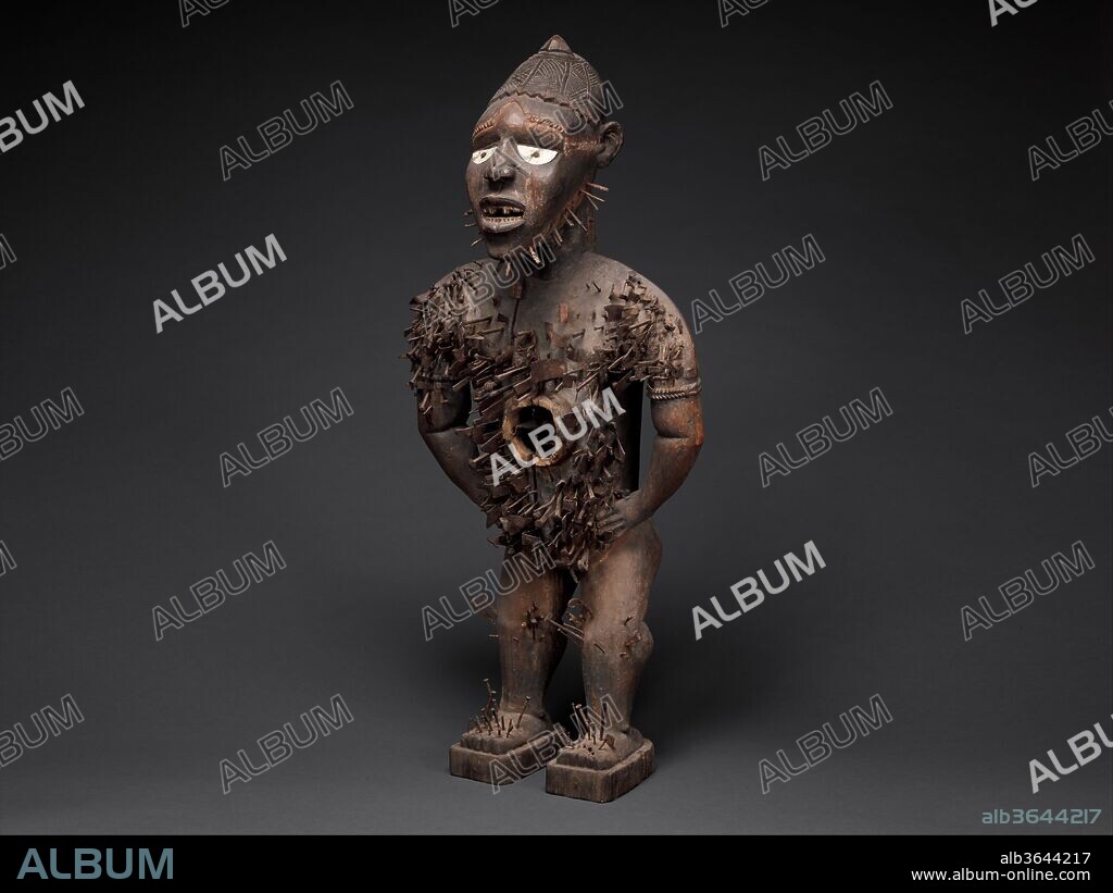 Power Figure (Nkisi N'Kondi: Mangaaka). Culture: Kongo peoples; Yombe group. Dimensions: H. 46 1/2 in. (118 cm), W. 19 1/2 in. (49.5 cm), D. 15 1/2 in. (39.4 cm). Date: 19th century.
Central African power figures are among the ubiquitous genres identified with African art. Conceived to house specific mystical forces, they were collaborative creations of Kongo sculptors and ritual specialists. This example belongs to the most ambitious class of that tradition, attributed to the atelier of a master active along the coast of Congo and Angola at the end of the nineteenth century and identified with Mangaaka, the preeminent force of jurisprudence.
That power was represented as a presiding authority and enforcing lord or king. Its crowning element is the distinctive mpu headdress worn by chiefs or priests. The figure's posture and gesture, leaning forward with hands placed akimbo on the hips, is the aggressive attitude of one who challenges fearlessly. Traces of a missing beard-a sign of seniority-survive in the form of nails along the contours of the chin. There are also vestiges of an abdominal cavity for medicinal matter that originally attracted the figure's defining force. The various metals embedded in the figure's expansive torso attest to its central role as witness and enforcer of affairs critical to its community. They document vows sealed, treaties signed, and efforts to eradicate evil. Ultimately, this work inspired reflection on the consequences of transgressing established codes of social conduct.