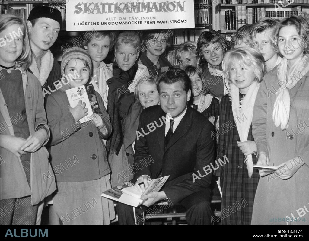 Orig. bildtext... LASSE LÖNNDAHL gästspelade häromdagen i sitt gamla yrke. Innan framgångarna på estraden, i radio och TV började var nämligen Lasse bokhandelmedhjälpare i en större bokhandel. Nu tyckte Lasse att det kunde vara roligt att återuppliva bekantskapen med läshungriga bokköpare igen och därför ställde han sig bakom disken i en tidigare kollegas affär i Högdalen. Lasse kunde glädja sig åt en ganska påträngande tillströmning av bokintresserade, större än vid hans tidigare framträdande bakom bokhandelsdisken. Han tyckte nog också att bokintresset hade spritt sig till de yngre grupperna. 13-10-60 Anm. Sångare Idoler Beundrare Fans Samtal Möten Ungdomsböcker Skattkammarön Fem-böckerna Bläddra Studiebesök Leenden Sjalar Sjaletter Autografer CD517 persons: LARS LÖNNDAHL sites: STOCKHOLM;SVERIGE.