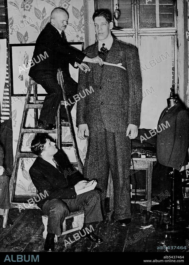 A Tall Order - Baine Myllyrinne, 8½ foot giant, being measured for a suit in Vienna, where he is training to become a boxer. Believe it or not, Baine Myllyrinne, eight and a half foot giant from Finland, needs 103 square feet of material to make him a suit. Was the tailor pleased. September 16, 1935. (Photo by Associated Press Photo).;A Tall Order - Baine Myllyrinne, 8½ foot giant, being measured for a suit in Vienna, where he is training to become a boxer. Believe it or not, Baine Myllyrinne, e.