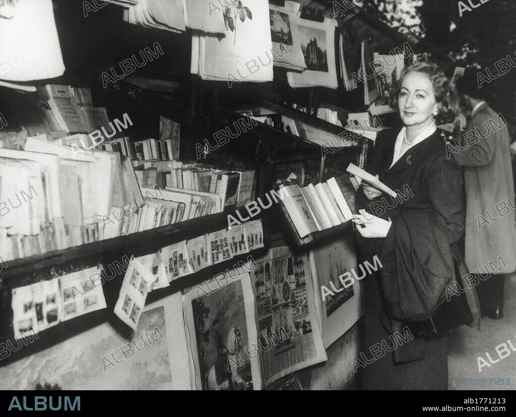 Alba de Céspedes holding a book near a bookstall. The Italian writer Alba de Céspedes y Bertini holding a book taken from a well-stocked stall selling literature and prints.