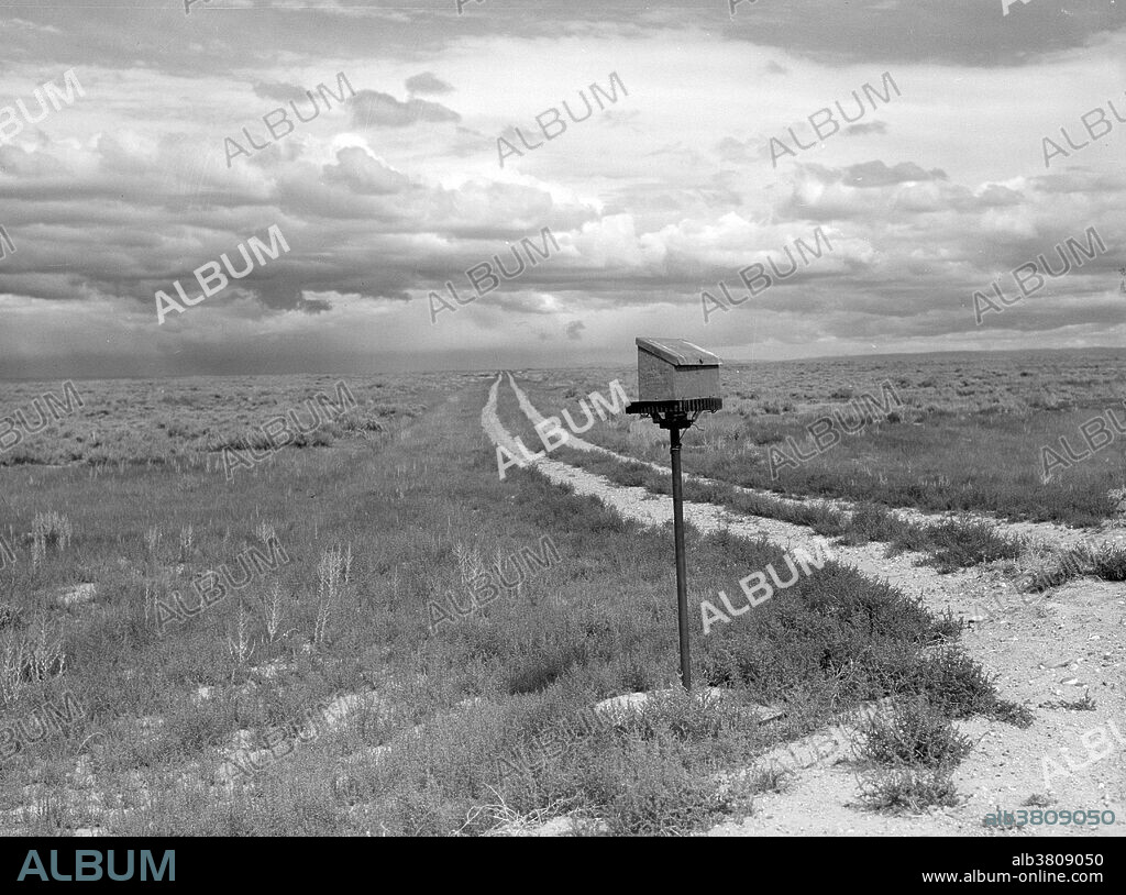 Entitled: "Ranch mailbox near Farson, Wyoming." Before the introduction of rural free delivery (RFD) by the Post Office in 1896, many rural residents had no access to the mail unless they collected it at a post office located many miles from their homes or hired a private express company to deliver it. For this reason, mailboxes did not become popular in rural America until curbside RFD mail delivery by the Post Office was an established service. In 1923 did the Post Office finally mandate that every household install a mailbox or mail slot in order to receive home delivery of mail. Originally designed only for incoming mail delivery, curbside mailboxes were soon fitted with a semaphore or signal flag mounted on an attached arm to signal the postman of outgoing mail, but also by the postman to inform the recipient that incoming mail had been delivered - a convenience to all during periods of freezing or inclement weather. Curbside mailboxes located on a rural route or road and sited at the intersection of the road with each recipient's carriageway or private drive allowed limited numbers of mail carriers to deliver mail to many widely scattered farms and ranches in a single day. Photographed for Farm Security Administration by Marion Post Wolcott, 1941.