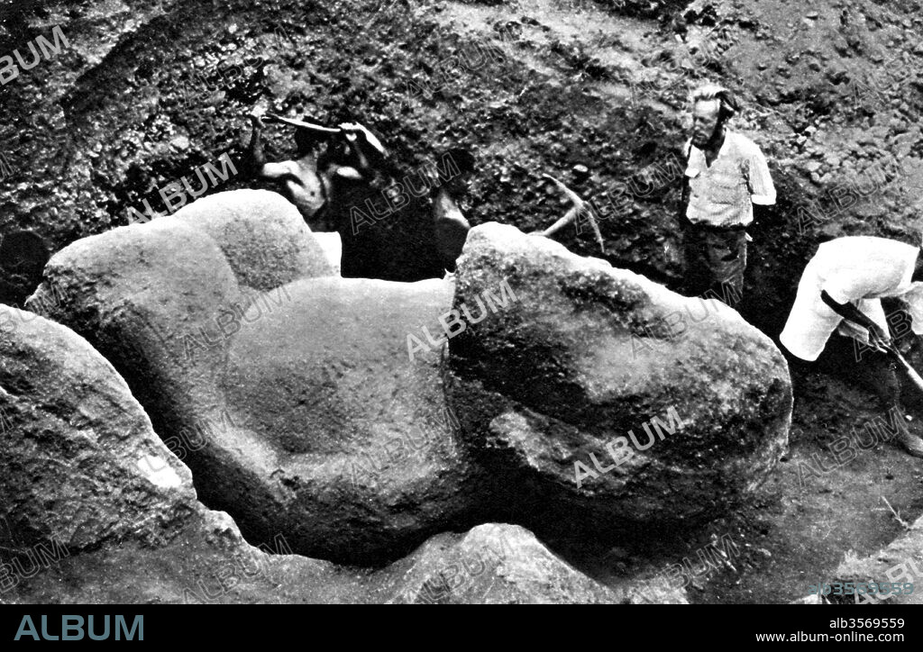 Moai are monolithic human figures carved by the Rapa Nui people from rock on the Polynesian island of Easter Island between the years 1250 and 1500. Nearly half are still at Rano Raraku, the main moai quarry, but hundreds were transported from there and set on stone platforms called ahu around the island's perimeter. Almost all moai have overly large heads three-eighths the size of the whole statue. The moai are chiefly the living faces (aringa ora) of deified ancestors (aringa ora ata tepuna). The statues still gazed inland across their clan lands when Europeans first visited the island, but most were cast down during later conflicts between clans. From 1955 through 1978, an American archaeologist, William Mulloy, undertook extensive investigation of the production, transportation and erection of Easter Island's monumental statuary. Photo originally captioned: Uncovering a hitherto unknown Easter Island colossal statue. A discovery made last November. Unlike previous known statues this is of red tuff. Published April, 1956.