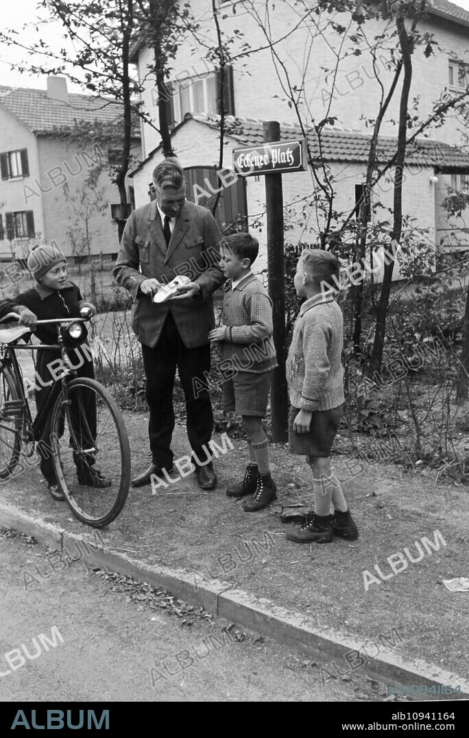 The mayor of Zeppelinheim and airship captain Hans von Schiller winding up the toy car of three boys on the street, near Frankfurt am Main, Germany 1930er.