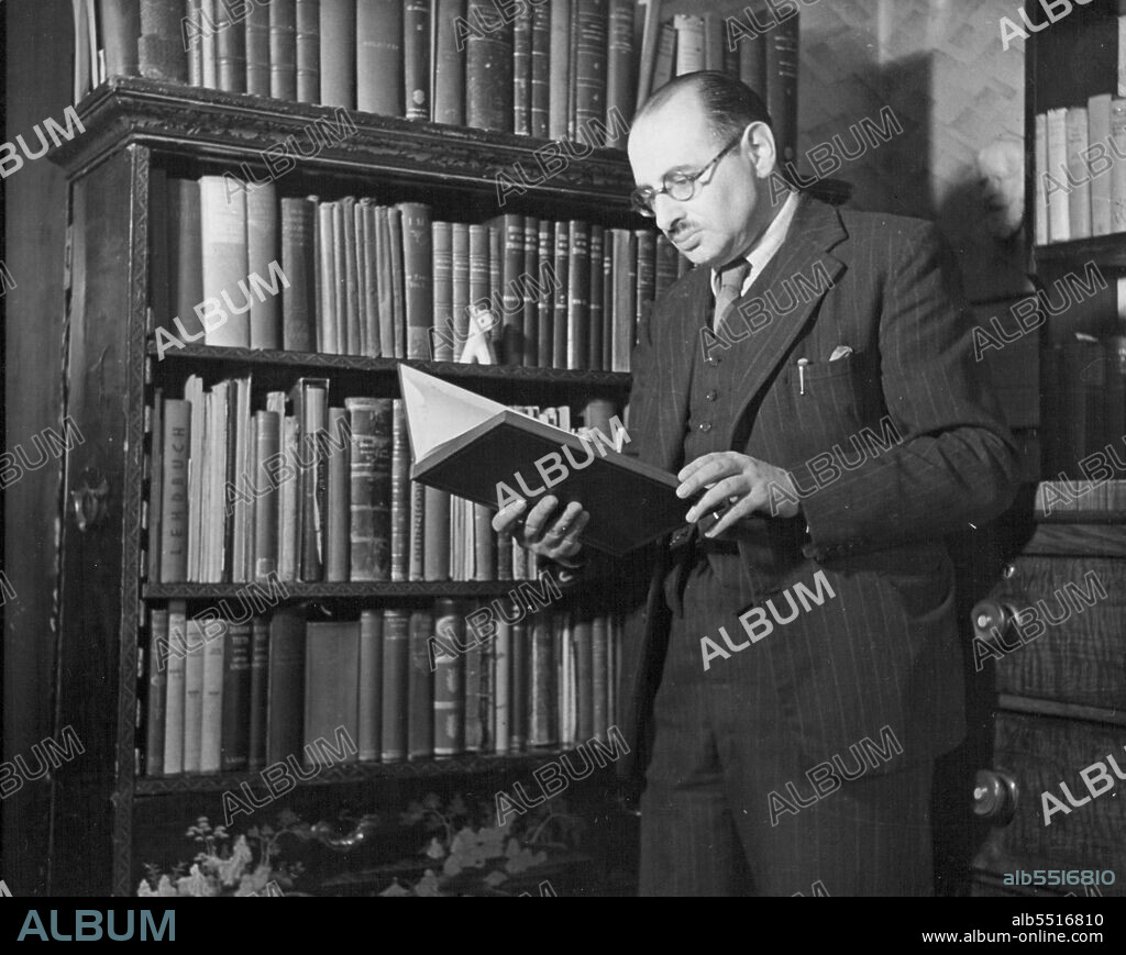 Shaw's Boswell - Frederick Loewenstein consults a volume from his library, Archibald. Henderson's "Shaw, playboy and Prophet"; every book is either by Shaw or has some bearing on him. Dr Loewenstein has the nearest thing to a complete collection of Shaw's writings that there is in existence, books, magazines old and new, tattered newspaper. He is a constant customer of secondhand booksellers; his bibliographer's eye has sought out many treasures,  including valuable first editions. Behind Dr Loewenstein, in the corner, hang a pair of woollen mittens, saved from Shaw's wastepaper basket when he had done with them (victim of had circulation, he wears them to keep his hands warm while writing). Shaw did not want them preserved; Loewenstein did not want them photographed. July 28, 1947. (Photo by Pictorial Press).