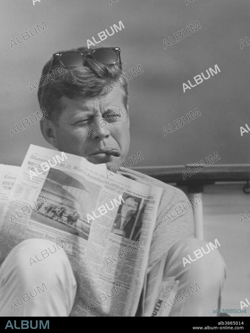 Digitally restored vintage photo of President John F. Kennedy relaxing outside, smoking a cigar and reading the newspaper.