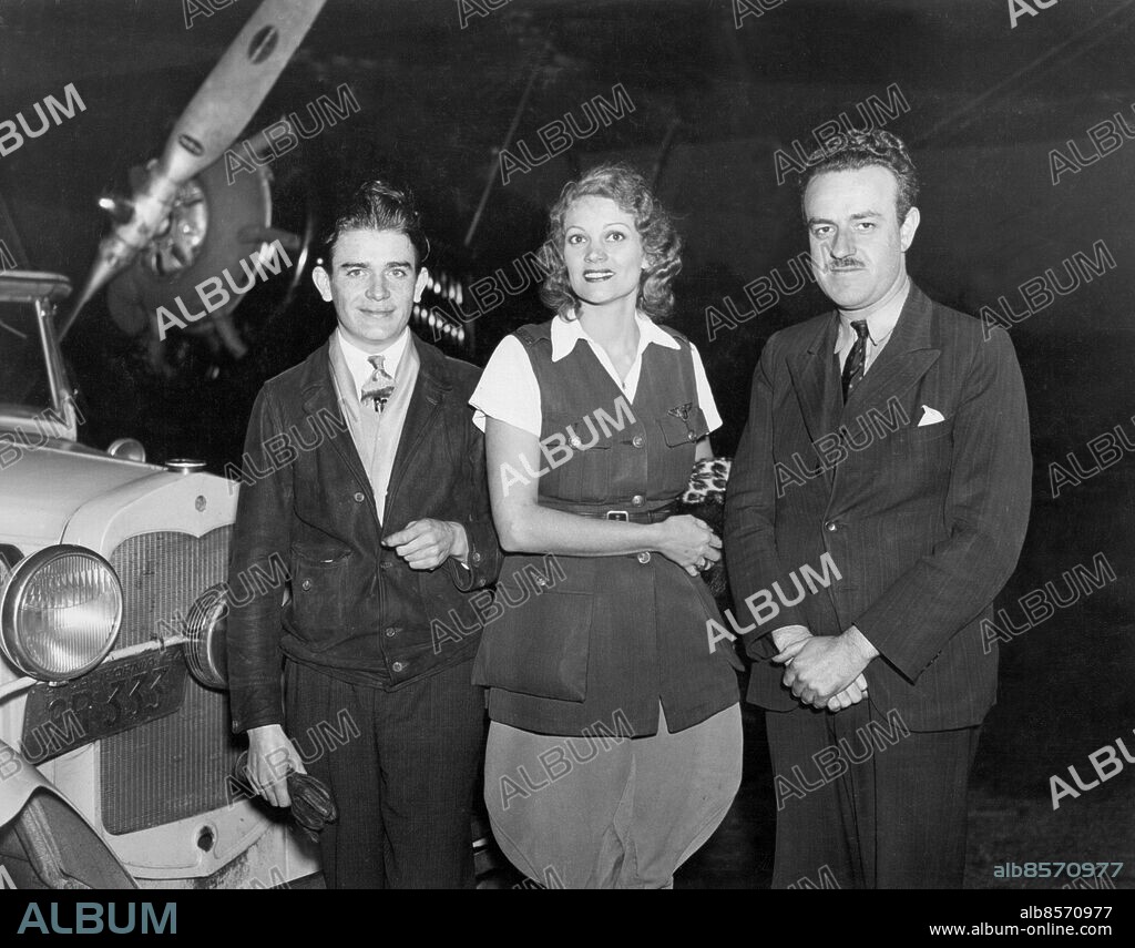 Orig. bildtext...ALOHA WANDERWELL BUYS PLANE FOR ROUND THE WORLD FLIGHT. On November 27th Aloha Wanderwell, of California purchased a plane with which she will make a round the world flight accompanied by her husband; and a former Australian aviator as navigator. The plane is a Wright J 6 Travelair, can seat three persons, has a thousand mile flying range. The trio who will make the flight are pictured at Roosevelt Field, L.I., when they bought the plane. Left to right - Walter Baker; his wife, Aloha Wanderwell; and Flight Lieut. A.J.R. Downes, navigator and co-pilot of Melbourne, Australia. Anm. Wanderwell, Aloha, 1908-1996, amerikansk globetrotter Aloha Wanderwells flicknamn var Galicia Hall. Hon var född i Kanada. Trio Leenden Billyktor CD410 persons: ALOHA WANDERWELL BAKER;WALTER BAKER sites: USA.