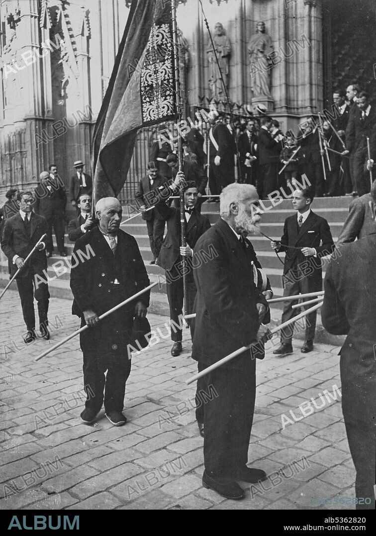 (19-06-1924): Gaudí leaving the Cathedral of Barcelona in front of the sign of the Artistic Circle of Sant Lluc - drawn by Alexandre de Riquer - in the procession of Corpus Christi. Behind Gaudí is the craftsman and member of the Cercle Artístic de Sant Lluc, Francesc Llauradó Gasol. The one who wears the banner is a son of Llimona and the one who pulls the string is a Dalmases Bocabella. The painter Darius Vilàs Fernández is walking down the stairs with the candle in his right hand. At the far right above the stairs was Josep Maria Jujol Gibert and beside him with his head peeled was Lluís Bonet Garí.
