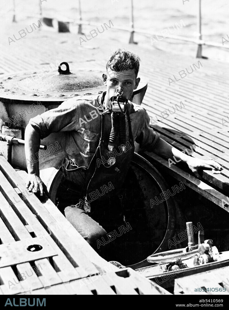 USS V-5 (SC-1) crewman A. L. Rosenkotter exits the submarine’s escape hatch wearing the Momsen Lung emergency escape breathing device during the submarine’s sea trials in July, 1930. The emergency breathing device was named for its inventor, U.S. Navy submarine rescue pioneer Commander Charles (Swede) Momsen. The submarine V-5 was later renamed USS Narwhal (SS-167). U.S. Navy, photographer unknown, 1930 (cropped and cleaned).