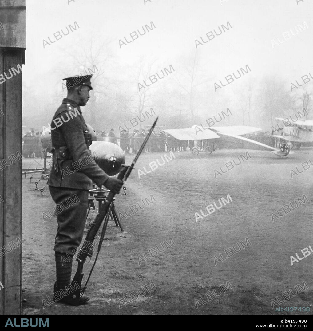 Magic lantern slide  WW1, 1914-1918, World war one images. Soldier standing guard. Standing with a gun with Fokker aircraft and torpedoes in the background. Display of captured German weapons and artillary at Horse Guards Parade, London 3rd November 1915.