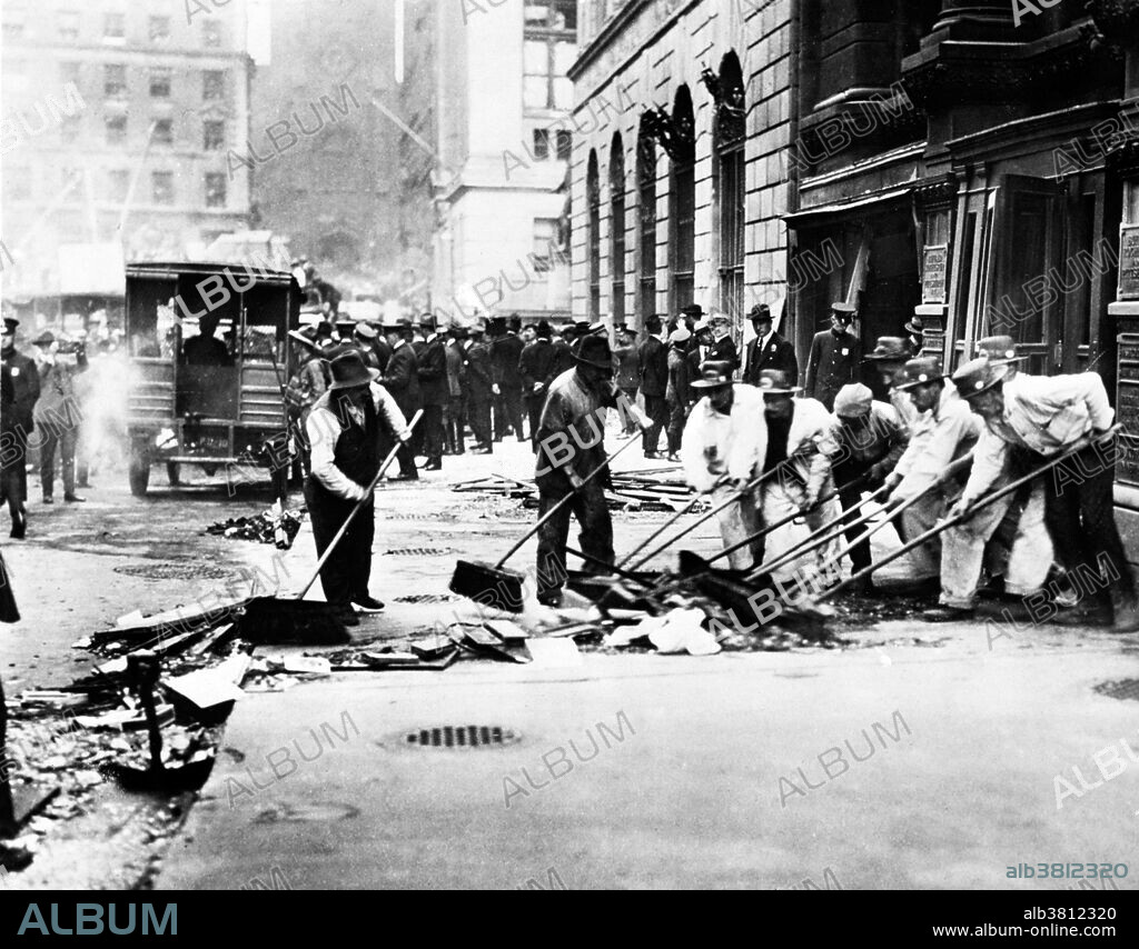 Entitled: "Sweeping up broken glass following Wall St. explosion ." Men with push brooms cleaning up rubble on sidewalk after explosion. On September 16, 1920, a horse drawn wagon stopped across the street from the headquarters of the J.P. Morgan bank at 23 Wall Street. Inside the wagon, 100 lbs of dynamite with 500 lbs of cast-iron sash weights exploded in a timer-set detonation. The horse and wagon were blasted into small fragments, but the driver was believed to have left the vehicle and escaped. The 38 victims, most of whom died within moments of the blast, were mostly young people who worked as messengers, stenographers, clerks, and brokers. The bomb caused more than $2 million in property damage ($23,500,000 with inflation) and destroyed most of the interior spaces of the Morgan building. There were 143 seriously injured, and the total number of injured was in the hundreds. The bombing was never solved, although investigators and historians believe the Wall Street bombing was carried out by Italian anarchists, a group responsible for a series of bombings the previous year. Photographed by the New York World-Telegram and the Sun Newspaper, 1920.