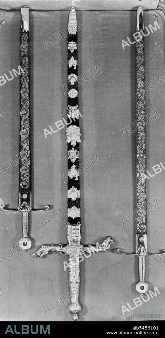 The Crown Jewels. The Three State Swords.
The Sword of State (in centre) is a two-handed Sword, the length of the blade being 32 inches. The handle is of gilt metal, the cross-pieces representing the Lion and the Unicorn. The Scabbard is decorated with diamonds, rubies and emeralds in designs of the Rose, the Thistle and the Shamrock.
At the Coronation the Peer who carries the Chamberlain, who in exchange hands over the Jewelled Sword.
The Sword on left is the Sword of Justice to the Spirituality, while the third sword is the sword of justice to the Temporality. September 01, 1952. (Photo by Sport & General Press Agency, Limited).