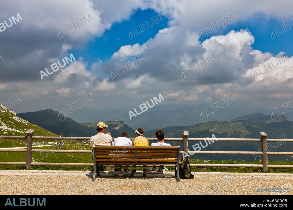 Funicular Railway between Malcesine and Mount Baldo (from 100 to 1760 metres): tourists sitting on a bench near the arrival station at Mount Baldo and watching le highland landscape.