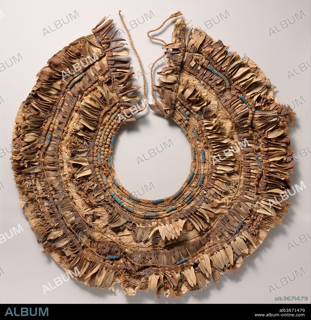 Floral collar from Tutankhamun's Embalming Cache. Dimensions: Diam. 47 cm (18 1/2 in.); W. 17 cm (6 11/16 in.); Diam. of disk beads 0.5 cm (3/16 in.). Dynasty: Dynasty 18. Reign: reign of Tutankhamun. Date: ca. 1336-1327 B.C..
This remarkably well preserved floral collar illustrates how the broad collars so frequently depicted in Egyptian tomb paintings were made. Alternating rows of flower petals and blossoms, leaves, berries, and blue faience beads were sewn to a papyrus backing, and linen ties secured the collar around the wearer's neck.  Some of the flora used in the Tutankhamun collars have been identified as olive leaves, cornflowers, and poppies.  Several collars in the cache were bound around the edge with red cloth, and the resulting combination of red, blue, black, and green must have been very colorful and similar to the polychrome decoration on some of the pottery jars in the same deposit.