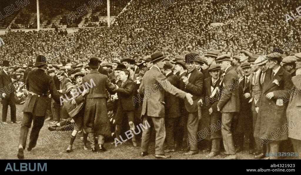 The first FA Cup Final is held at the new Wembley Stadium in London, 28 April 1923, (1935). Police trying to keep the crowds back at the first Football Association Challenge Cup final match between Bolton Wanderers and West Ham United. 'The crowds were so enormous that they broke down the barriers and the police had to form cordons to prevent spectators overflowing on to the ground.' From "The Silver Jubilee Book - The Story of 25 Eventful Years in Pictures". [Odhams Press Ltd., London, 1935].