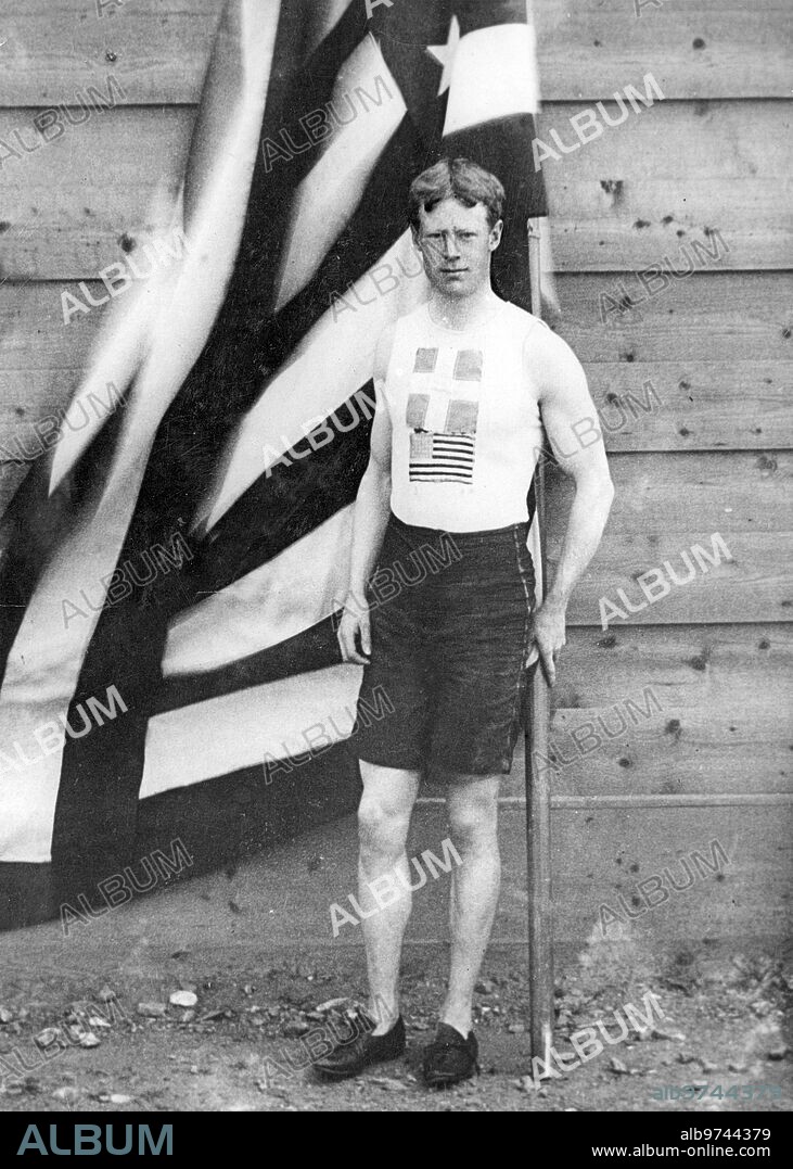 Atenas (Grecia), 10/04/1896. El atleta norteamericano Thomas Pelham Curtis posa junto a la bandera de su país en los Juegos Olímpicos, donde conseguirá la medalla de oro en los ciento diez metros vallas.