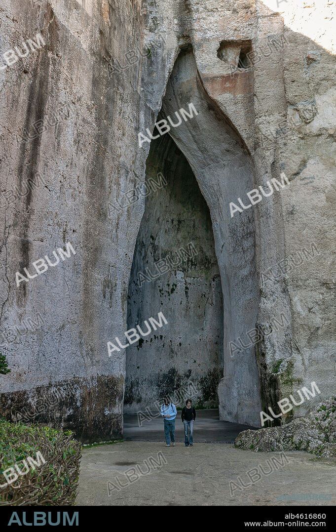 Syracuse, The Archaeological Park of the Neapolis of Syracuse: the entrance to the Ear of Dionysius (or Dionysus).. The Ear of Dionysius (or Ear of Dionysius) is an artificial cave located in the ancient stone quarry called the Latomia of Paradise, under the Greek Theatre of Syracuse. Excavated in limestone, it is about 23 m high. and 5 to 11 m. wide, and 65 m. deep, with an S-shape that makes it a place of acoustic amplification of sounds (up to 16 times).. According to the legend, Caravaggio gave it its name. According to tradition, the tyrant Dionysius had the cave excavated and he locked up the prisoners and he listened to their speeches.