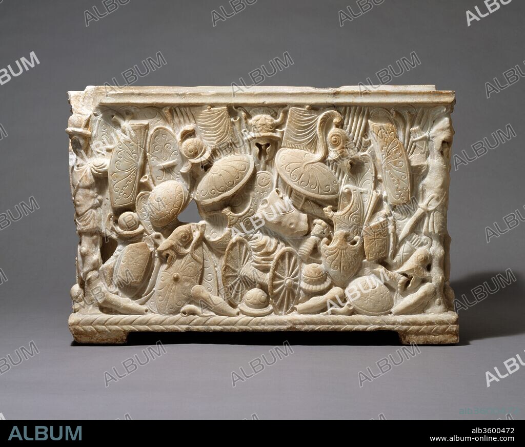 Marble cinerary urn. Culture: Roman. Dimensions: Overall: 14 1/4 x 21 1/4 x 16 1/8 in. (36.2 x 54 x 41 cm). Date: 1st half of 1st century A.D..
This Roman cinerary urn is highly unusual in having the spoils of war as its principal theme. Despite the fragmentary nature of the piece, the trophies and piles of weapons and armor that cover the back and sides of the rectilinear box are very striking. In both detail and composition, the panels are representative of high-quality workmanship, suggesting that the work was a special commission. Sadly, much of the front, where the inscription recording the name of the deceased would have been, is missing. The urn is said to have been excavated from a tomb near Anagni, southeast of Rome, in 1899. 
Other marble funerary urns in the Museum's collection (see 96.9.222a, b; 25.78.29; and 27.122.2a, b; on display in the courtyard) belong to much more common types of Roman funerary art, cinerary urns that either resemble actual receptacles (vases or baskets) or are in the form of altars or miniature buildings. In both iconography and craftsmanship, the present urn foreshadows the elaborate sarcophagi of the Mid-Imperial period.