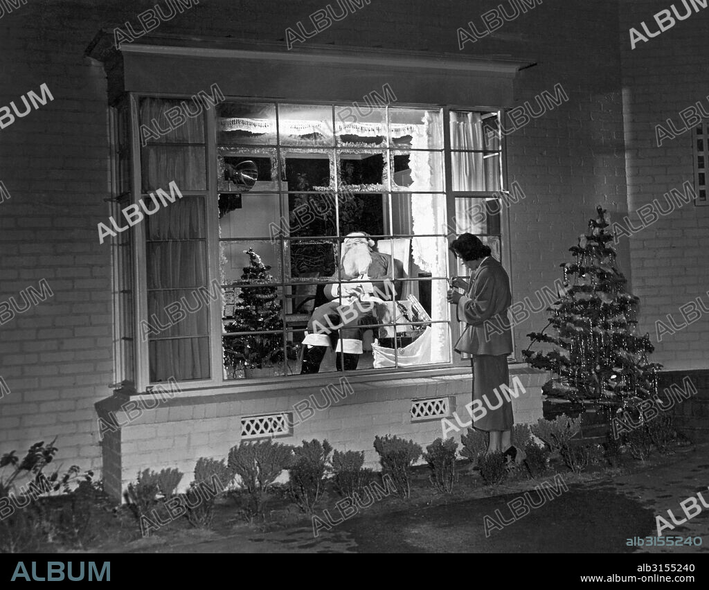 Beverly Hills, California:  December 22, 1949. This Beverly Hills resident is putting the finishing touches on her Christmas window decoration of Santa asleep in a chair.