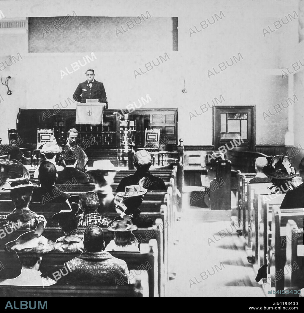Black and white historic image of a preacher in a pulpit and the congregation in the wooden pews.