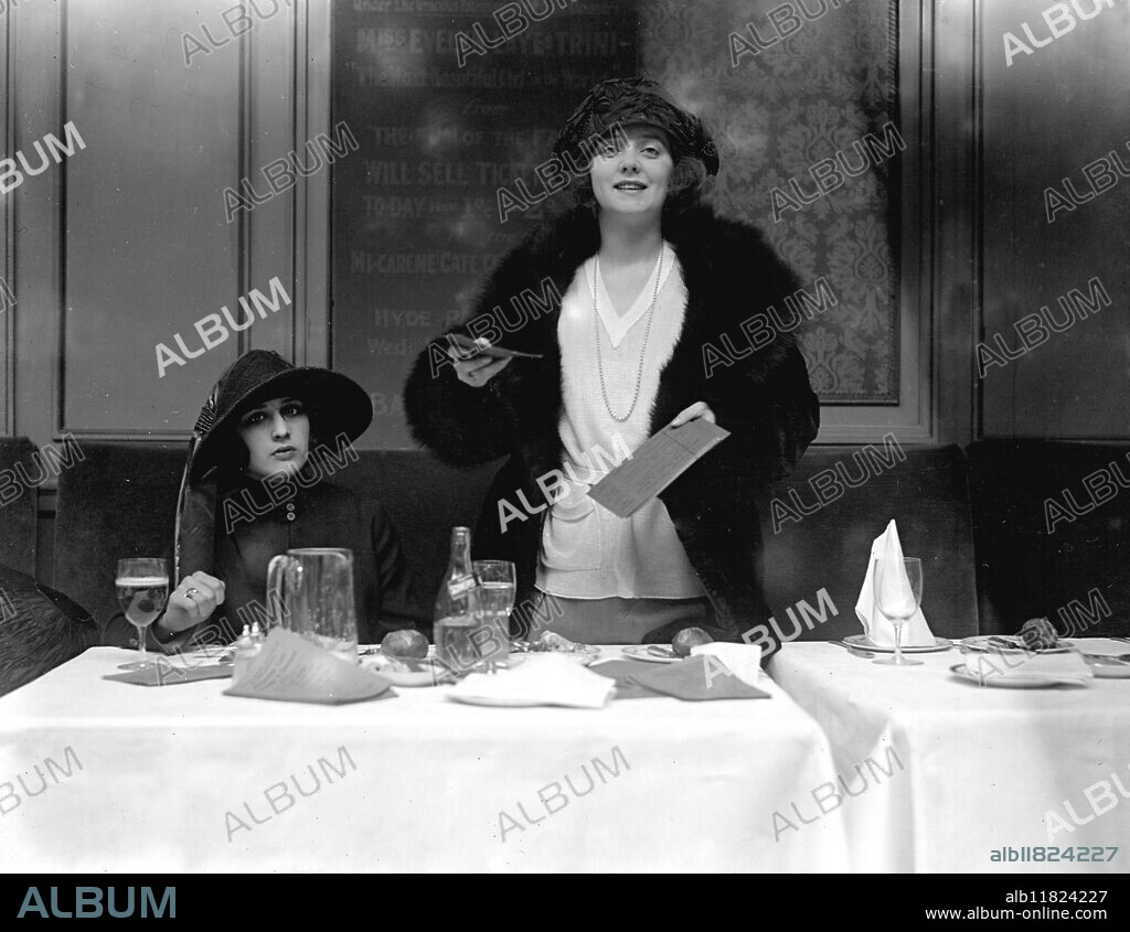 Charming auctioneer for Charity . Actress , Miss Evelyn Laye ( 1900 - 1996 ) , supported by ' Trini , the most beautiful girl in the world ', auctioning tickets at the Embassy Club for the Mi Careme Cafe Chantant and Dansant to be held at the Hyde Park Hotel in aid of Babies Welfare Homes , London , England . 1920s.