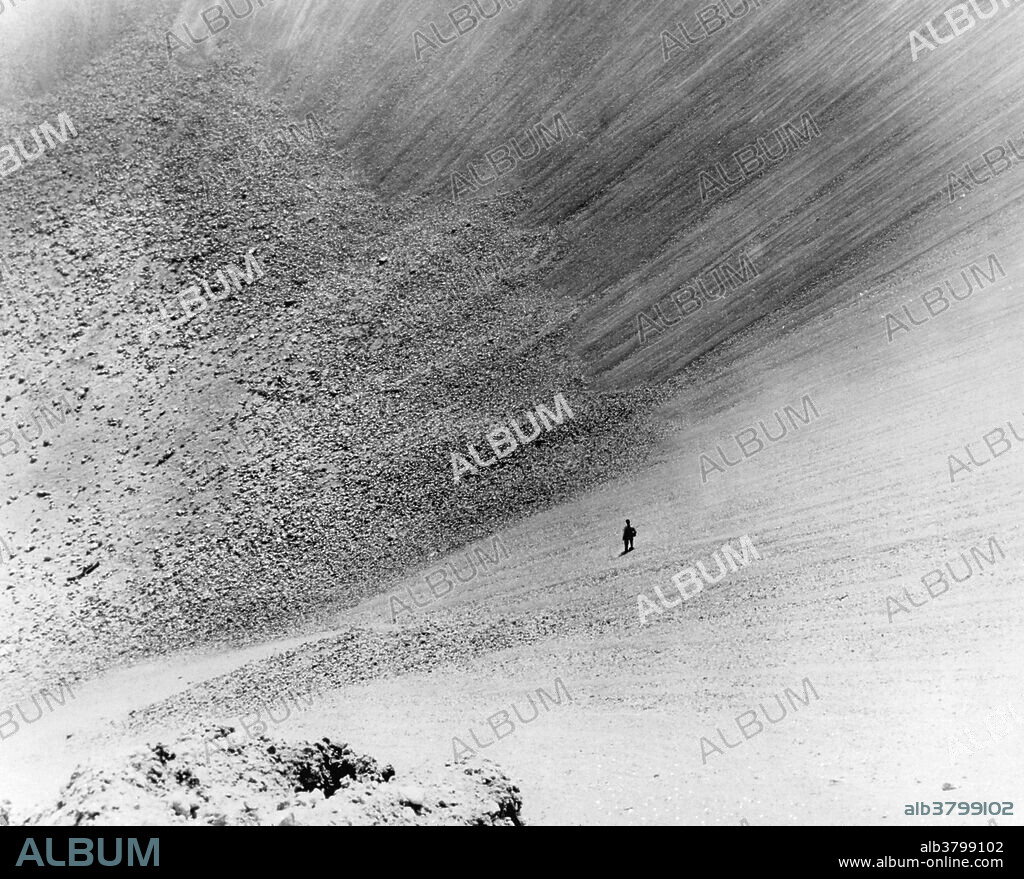Storax Sedan, an underground 100-kiloton thermonuclear test conducted at Nevada Test Site on July 6, 1962 as part of Operation Plowshare, was a program designed to develop peaceful uses for nuclear explosives, such as canal and harbor building. Sedan left the largest man-made crater in the United States, displacing 12 million tons of earth and measuring 320 feet deep by 1280 feet in diameter. The first descent to the floor of the crater was made the following February. It took 15 minutes to climb down and an hour to climb back up. The man pictured is Lloyd Guymon, the descent party's photographer.