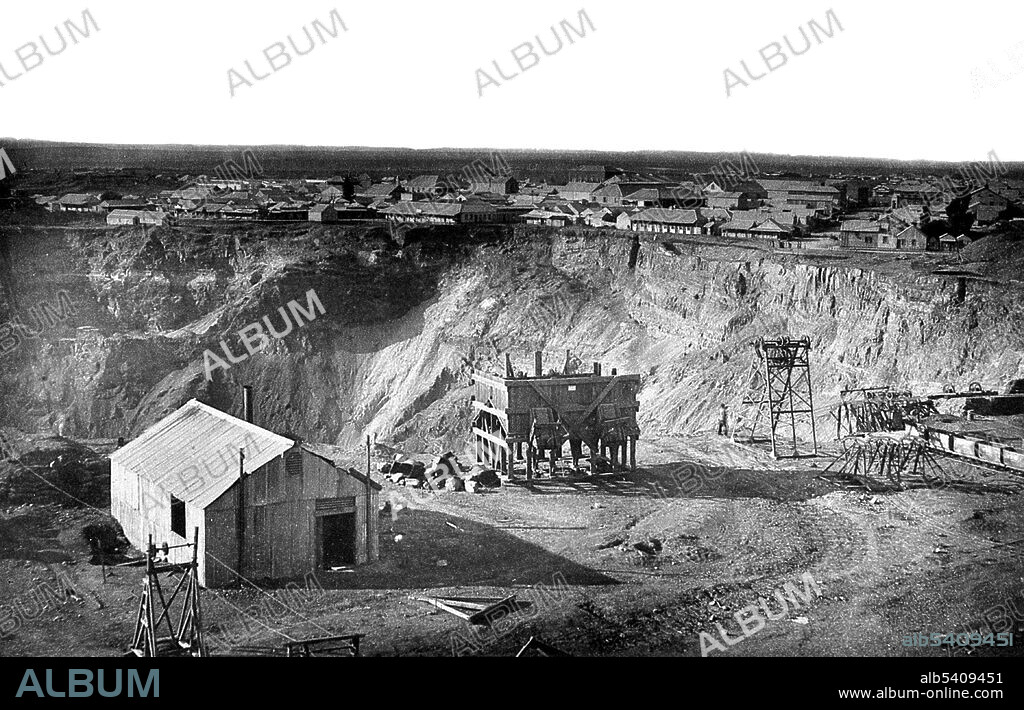 Entitled: "Kimberley mine and town." The 1867 discovery of diamonds in the Cape Colony, South Africa, radically modified not only the world's supply of diamonds but also the conception of them. The first diamond discoveries in South Africa were alluvial. By 1869, diamonds were found far from any stream or river. First in yellow earth and below in hard rock called blue ground, later called kimberlite, after the mining town of Kimberley. In the 1870s and 1880s Kimberley, encompassing the mines that produced 95% of the world's diamonds, was home to great wealth and fierce rivalries. In 1872, one year after digging started, the population of the camp of diggers grew to around 50,000. As digging progressed, many men met their deaths in mining accidents. The unsanitary conditions, scarcity of water and fresh vegetables as well as the intense heat in the summer, also took their toll. In 1888 the leaders of the various mines decided to amalgamate the separate diggings into one big mine and one big company known as De Beers Consolidated Mines Limited. The Kimberley Mine is an open-pit and underground mine in Kimberley, South Africa, and claimed to be the largest hole excavated by hand, although this claim is disputed. Robert Harris, 1888.