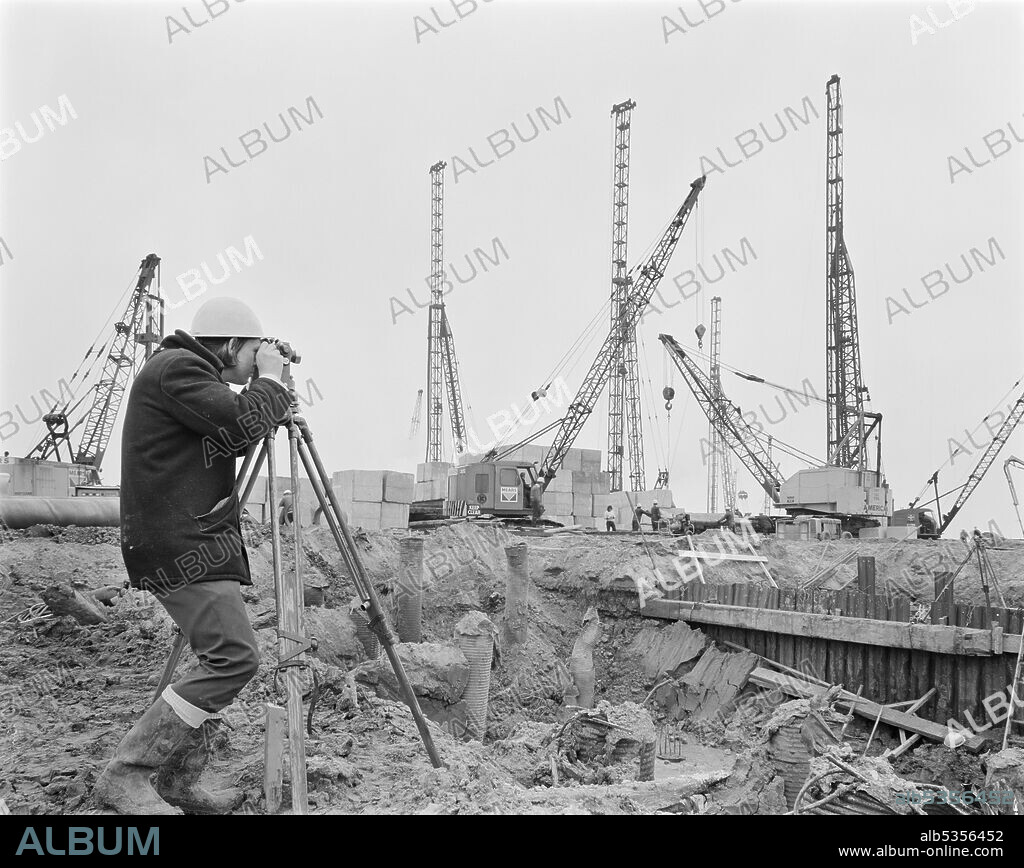 JOHN LAING PLC. A Laing surveyor using a theodolite on the construction site of the Isle of Grain Power Station. The Isle of Grain Power Station was an oil fired power station built in the 1970’s by multiple contractors, including John Laing and Son Ltd. When the power station opened in 1979, it had the second tallest chimney in the UK at 244 metres high. The power station has now been demolished and the chimney was destroyed in September 2016. A new Combined Cycle Gas Turbine (CCGT) power station has been built at the site.