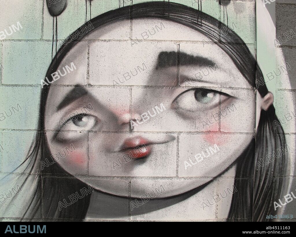 Ilustración de cara de mujer redonda con grandes ojos soñadores sobre pared de ladrillo; graffiti mural, Plaza de las Glorias; Distrito San Martin, Barcelona en 2014.