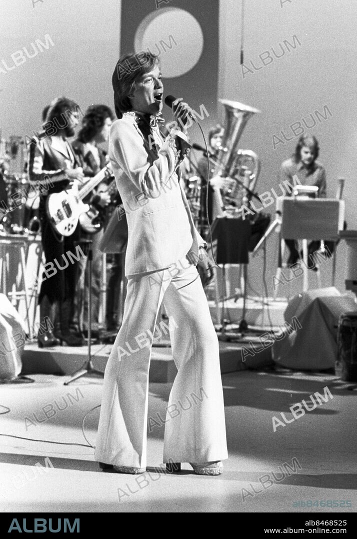 ARKIV 1975. Sångaren och artisten Björn Skifs med sitt kompband Blåblus i bakgrunden uppträder i SVT:s underhållningsprogram Nöjeshallen som sändes i SVT TV 1 1975-05-10.. Foto: SVT / Kod: 5600. utsvängda byxor, platåskor, vit smoking. Bildservice E 232 / Sv/v neg.