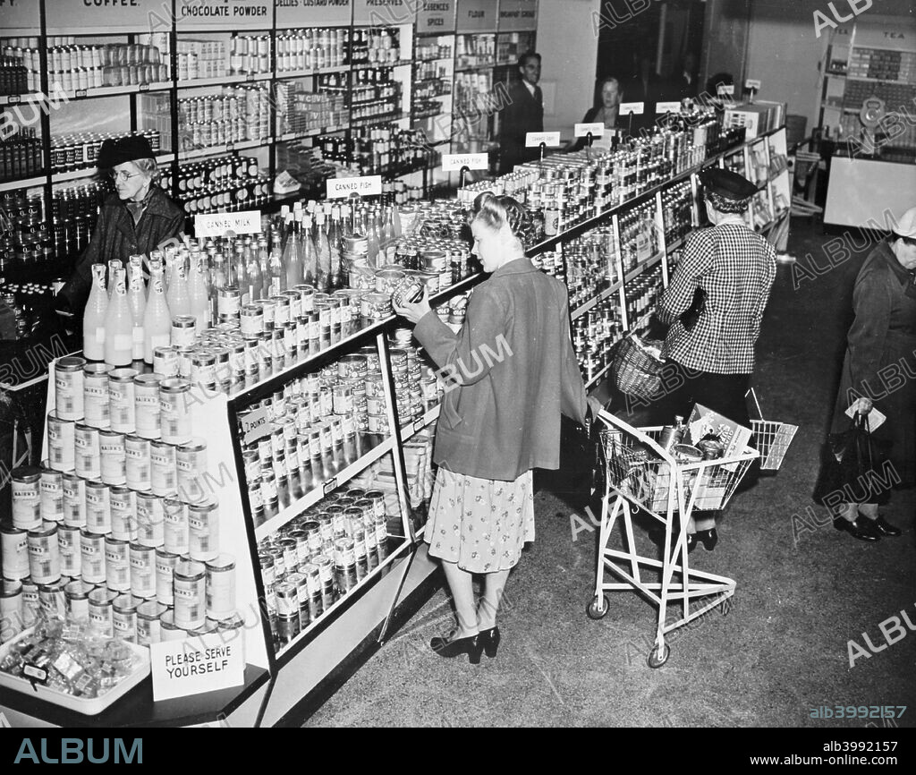 Lyons staff store, Cadby Hall, West Kensington, London. The self service grocery department. Women peruse the neatly stacked shelves of tinned food and bottled drinks.