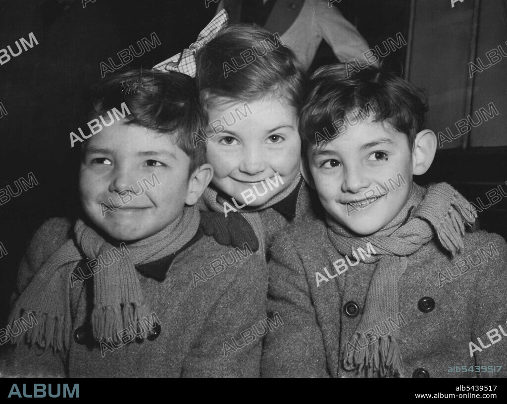 The 'Kenton Triplets' Go To Tasmania -- Three young migrants, the seven-year-old Tonelly triplets (left to right) Paul, Julia and Peter - pictured at Waterloo Station, London, before boarding the 'Malaja' boat train for Australia today (Thursday). Born on St. Valentine's Day seven years ago, they are from Kenton, Middlesex, and are going with their parents to settle in Northern Tasmania. Mr. Walter Tonelly, the father, has been cattle herdsman to the Earl of Wilton, at Woodstock, Oxford. He will.