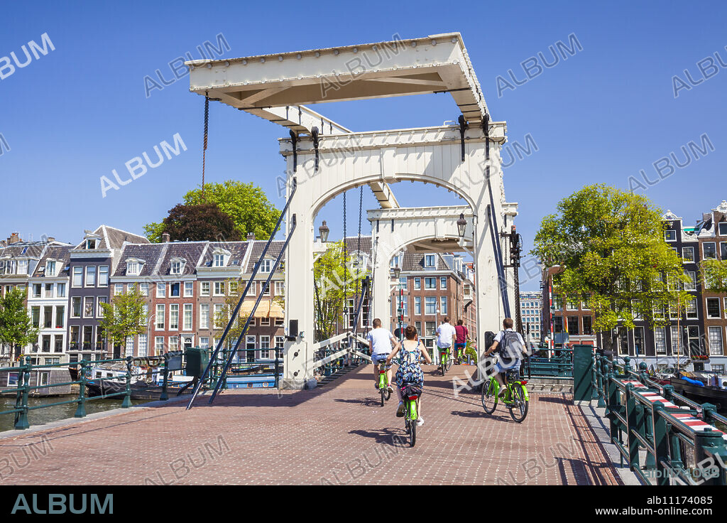 Cyclists riding across the Magere brug (Skinny Bridge) spanning the River Amstel, Amsterdam, North Holland, Netherlands, Europe.
