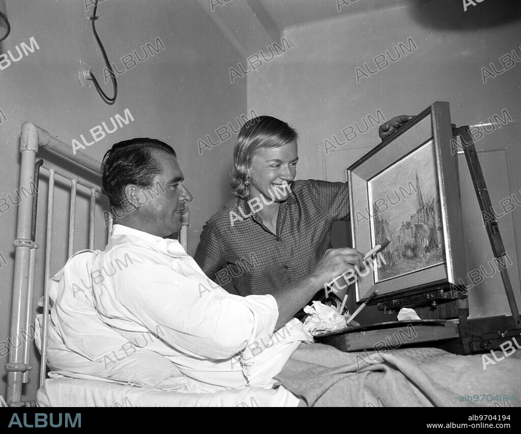 Ex-Coldstream Guards Major Alexander Beattie , watched by his wife , 32 year old Lady Rozelle Beattie , catches up on his painting during his stay at the London Clinic . Lady Beattie , just returned from a 1200 mile trip to Russia in her two ton yacht Martha McGilda , rushed straight to the clinic after receiving a message at sea about her husband's illness , and found him sitting up in bed .He had a major internal operation . 36 year old Major Beattie , an artist , expects to be in hospital convalescing a further ten days . 25 September 1959.