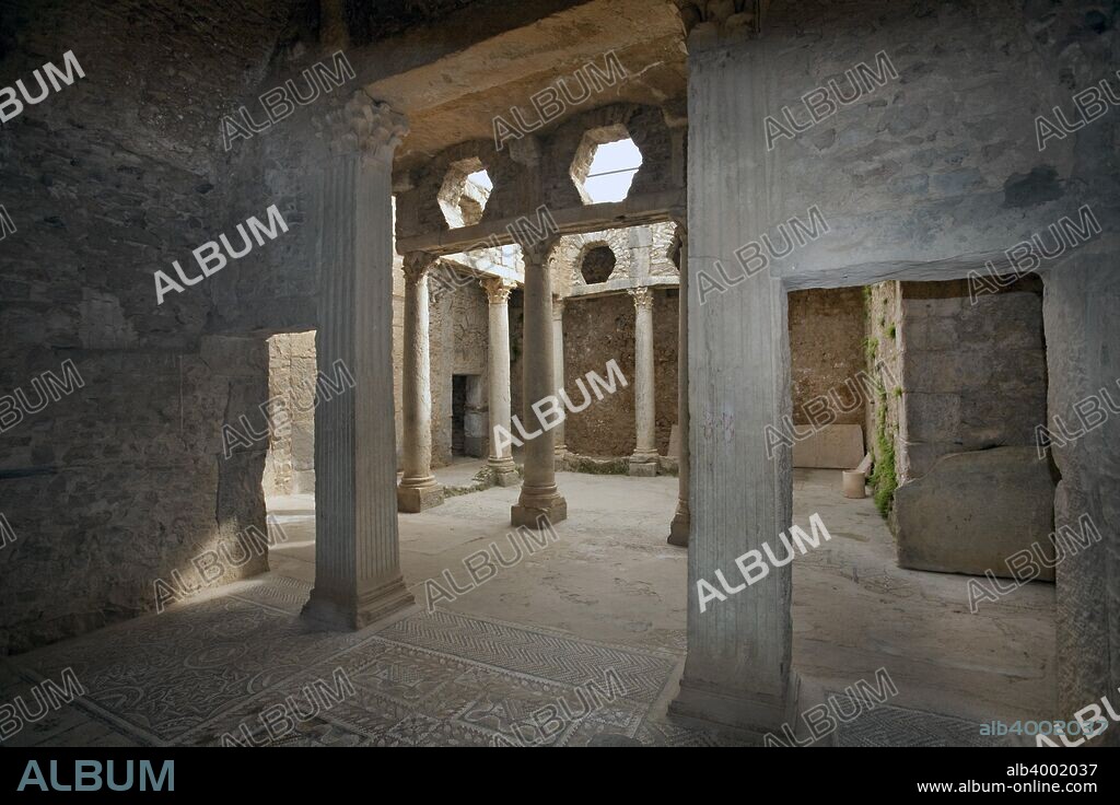 The House of the Hunt, Bulla Regia, Tunisia. The House of the Hunt, which takes its name from a mosaic in the basement, evidently belonged to a wealthy citizen. It was constructed by combining and altering a number of small existing houses. The upper floor is badly ruined, but the basement, lying some 5m (16ft) below ground level, is well preserved. The rooms, laid out round a courtyard lined with Corinthian columns, include bedrooms (identified by the small mosaic-decorated platforms for the beds) and a large dining room (triclinium), also with a pavement mosaic. The bedrooms have an interesting air supply and ventilation system, with pipes built into the walls which communicate with an air shaft surrounding the rooms. The layout on the ground floor is similar, with two colonnaded courtyards, dining and living rooms, bedrooms and a small bath-house. Bulla Regia is an archaeological site in northwestern Tunisia, a former Roman city near modern Jendouba. It is noted for its Hadrianic-era semi-subterranean housing, a protection from the fierce heat and effects of the sun.