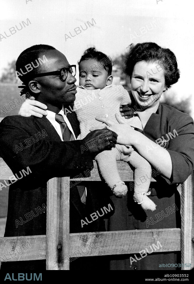 Living For Africa -- Mr. and Mrs. Appiah seen with their baby son Kwame at Frith Hill Oakridge near Stroud (Glos) where they are staying with Dame Isobel Cripps, widow of the late Sir Stafford Cripps, prior to sailing for Africa. Mrs. Appiah was formerly Peggy Cripps, daughter of Sir Stafford and Lady Cripps.Mr. and Mrs. Appiah, daughter and son-in-law of the late Sir Stafford Cripps are sailing to Africa later this week with their baby son Kwame. They are at present staying with Dame Isobel Cripps, widow Sir Stafford, at her Cotswold home Firth Hill at Oakridge near Stroud (Glos). November 15, 1954. (Photo by Fox Photos).